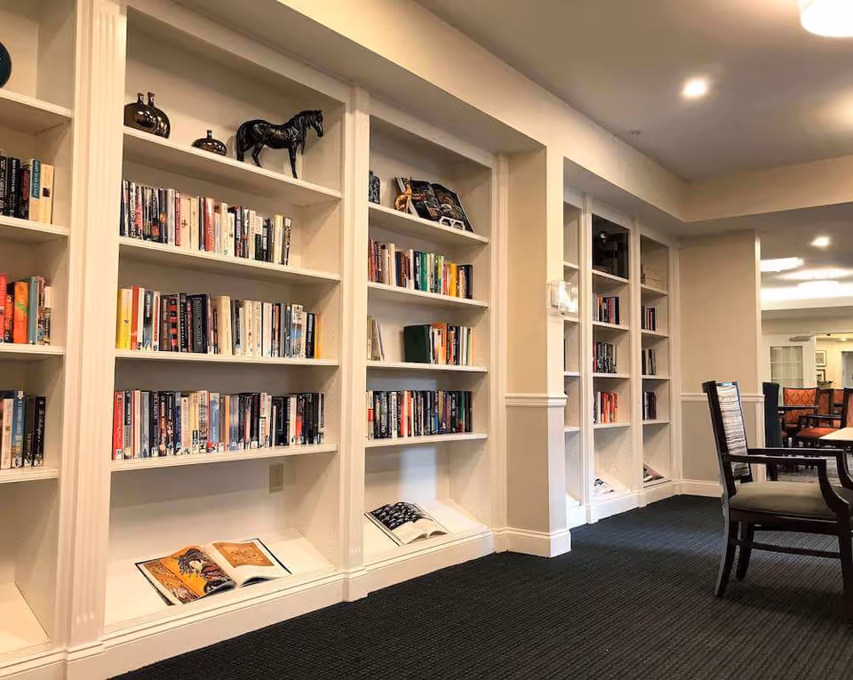 Well-lit interior reading area with built-in white bookshelves filled with books and a table and chairs to the right.