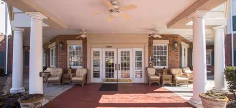 Entrance to Brookdale South Charlotte with white columns, brick exterior, glass doors, and seating.