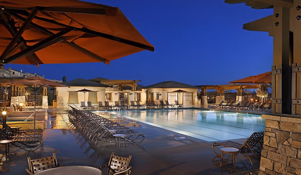 Outdoor swimming pool and lounge area with umbrellas and cabanas at dusk.
