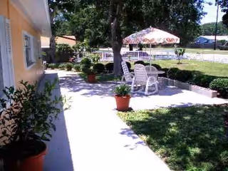Outdoor patio of a senior facility with white plastic chairs, umbrella, planters, and a yellow building.