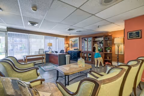 Reception lobby with arranged armchairs, a central coffee table, a receptionist desk by large windows, and a decorative bookshelf with a giraffe statue.