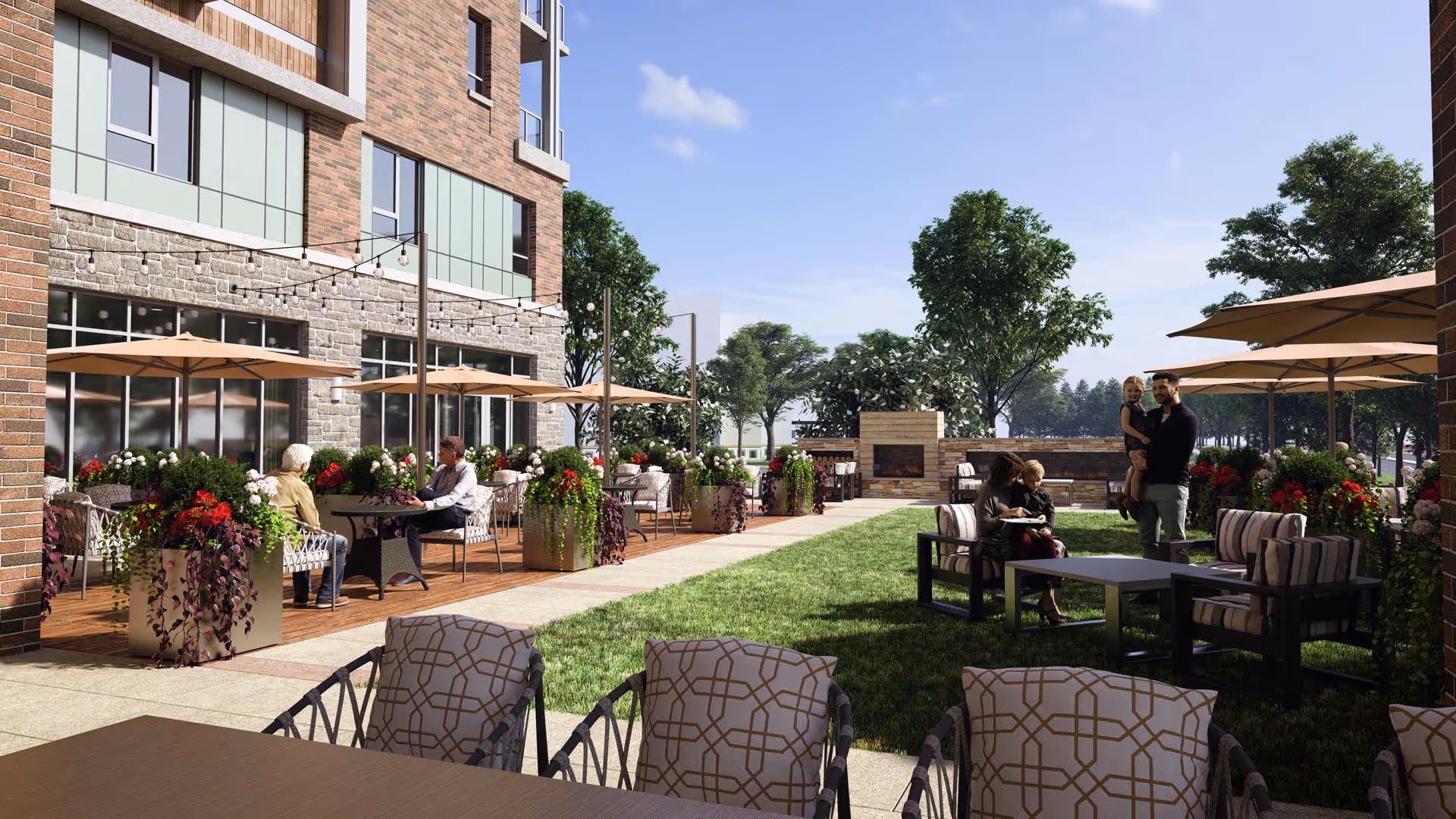 Outdoor patio area at The Seneca Rockville featuring seating with tables and umbrellas, potted plants with flowers, and a grassy lawn with additional seating. Several people are enjoying the space, including two individuals sitting at a table and a family with children near a fireplace in the background. The building exterior is visible with brick and stone walls and large windows.