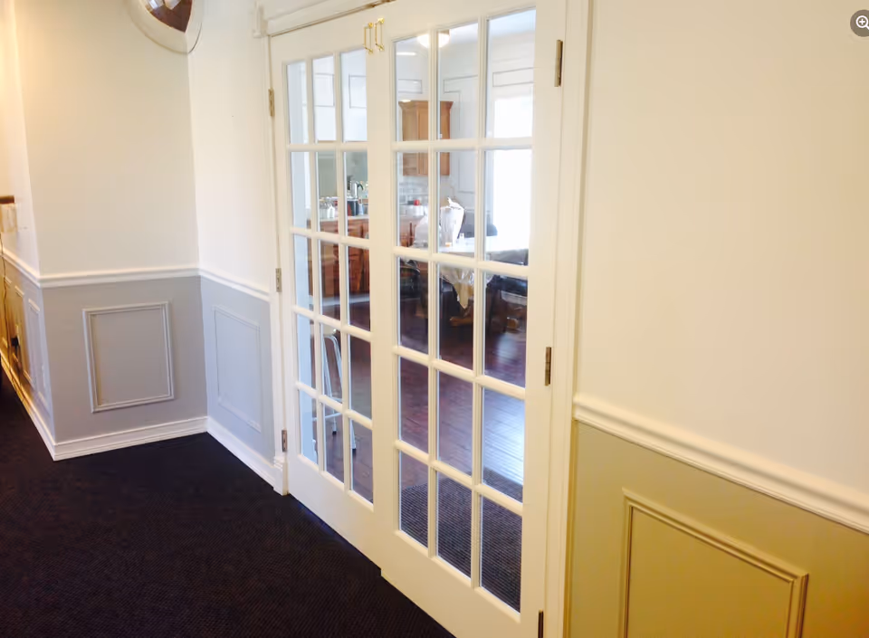 Hallway with white French double doors opening into a bright living area, featuring wainscoting and dark carpet.