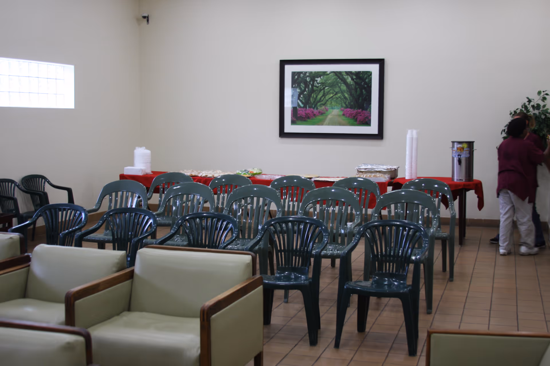 Interior meeting/dining room with rows of green plastic chairs facing a buffet table against a wall under framed artwork.