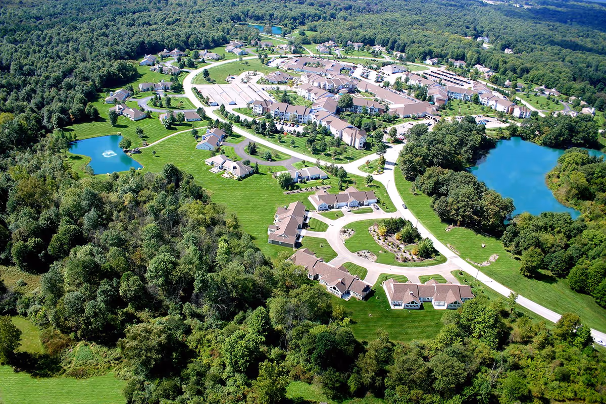 Aerial view of Laurel Lake Retirement Community showing multiple residential buildings, roads, green lawns, trees, and two ponds with fountains surrounded by forested areas.