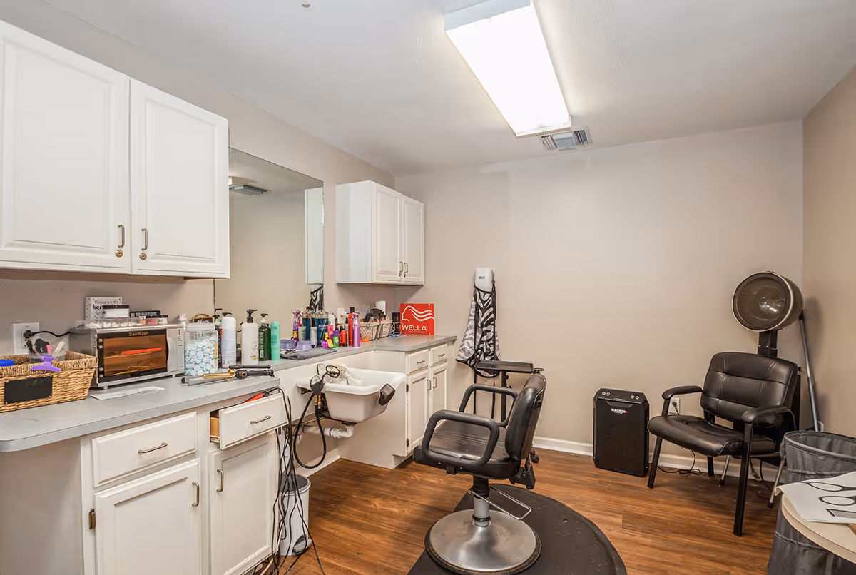 Interior salon-style room with styling chairs, a wash sink, cabinets, and hair products on a counter.