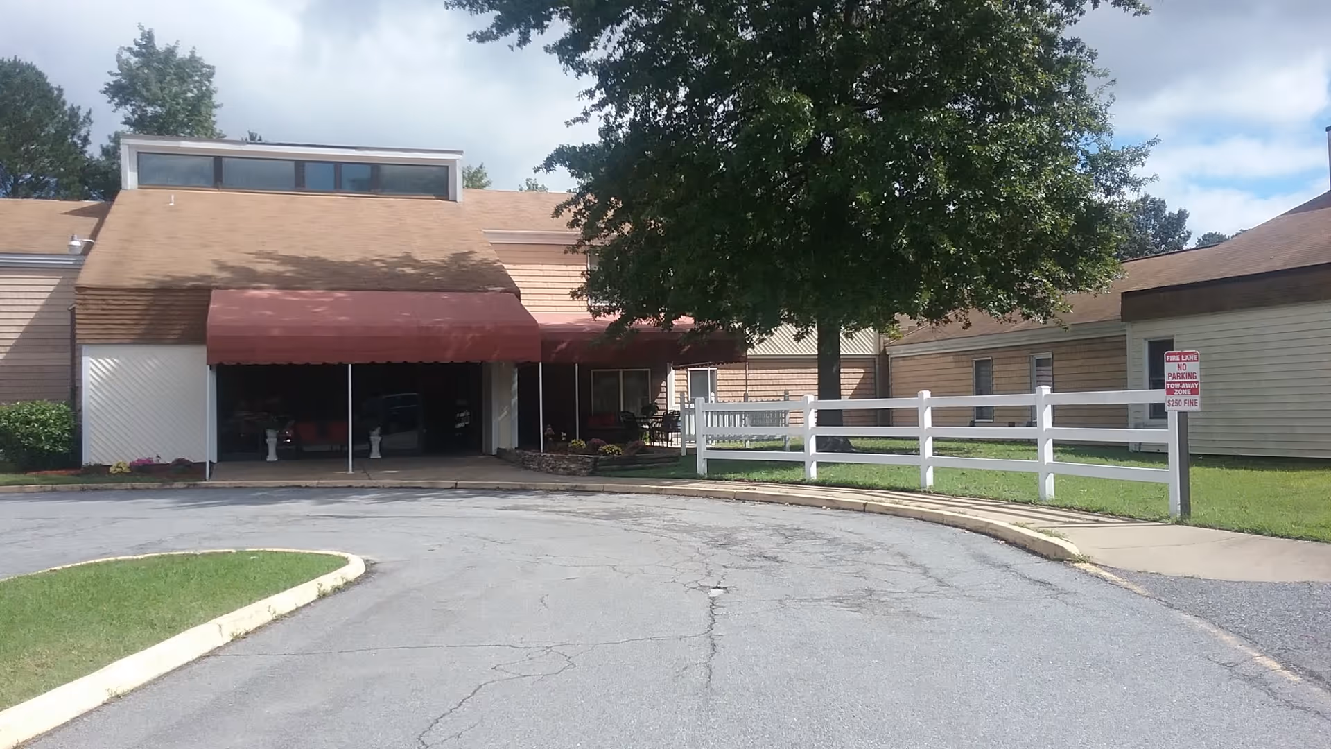 Front exterior view of Parsons Residential Care Center showing a building with a brown roof, a red awning over the entrance, a large tree, white fence, and a curved driveway.