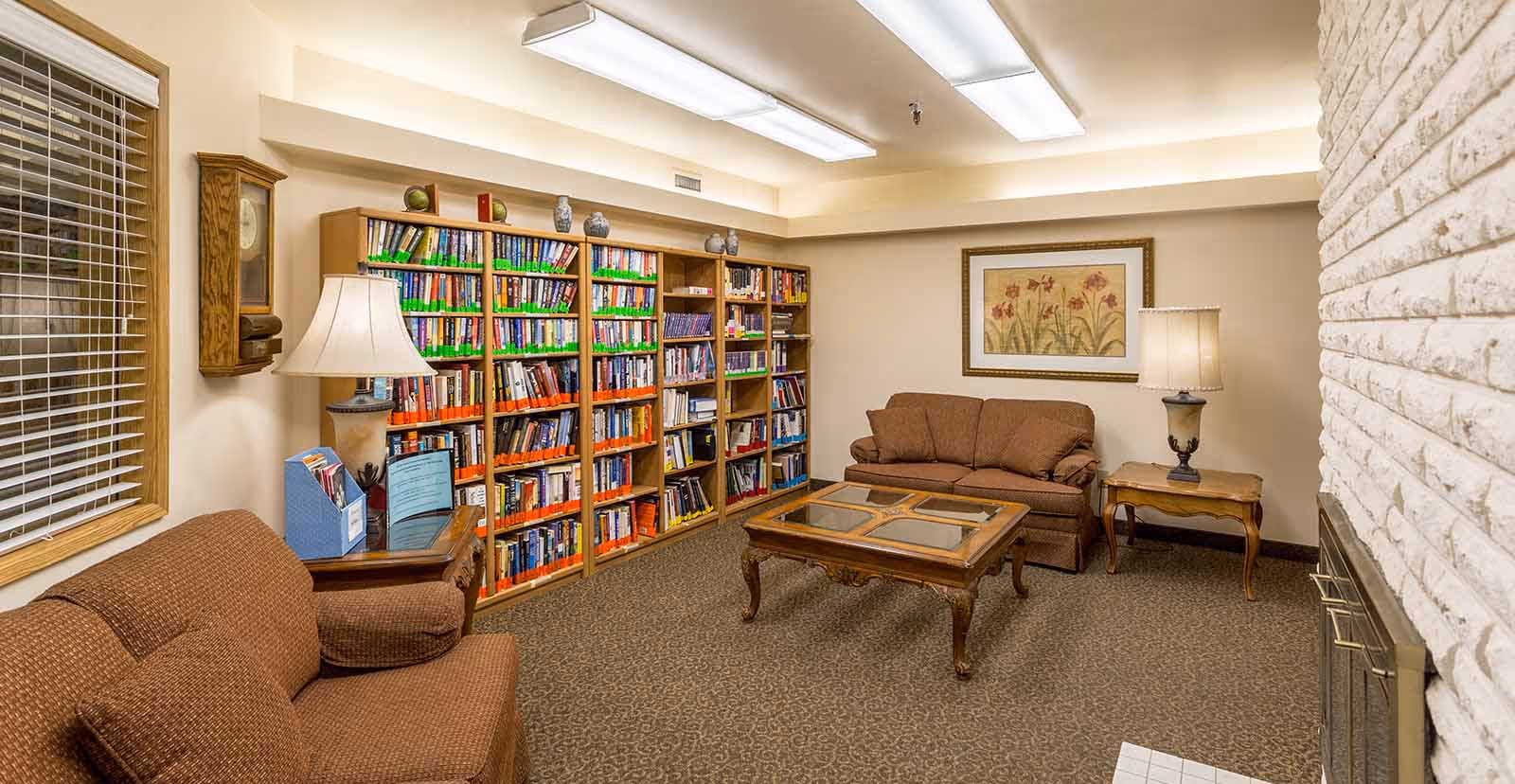 Cozy common room with sofas, a coffee table, bookshelves lining the back wall, lamps, and a fireplace.
