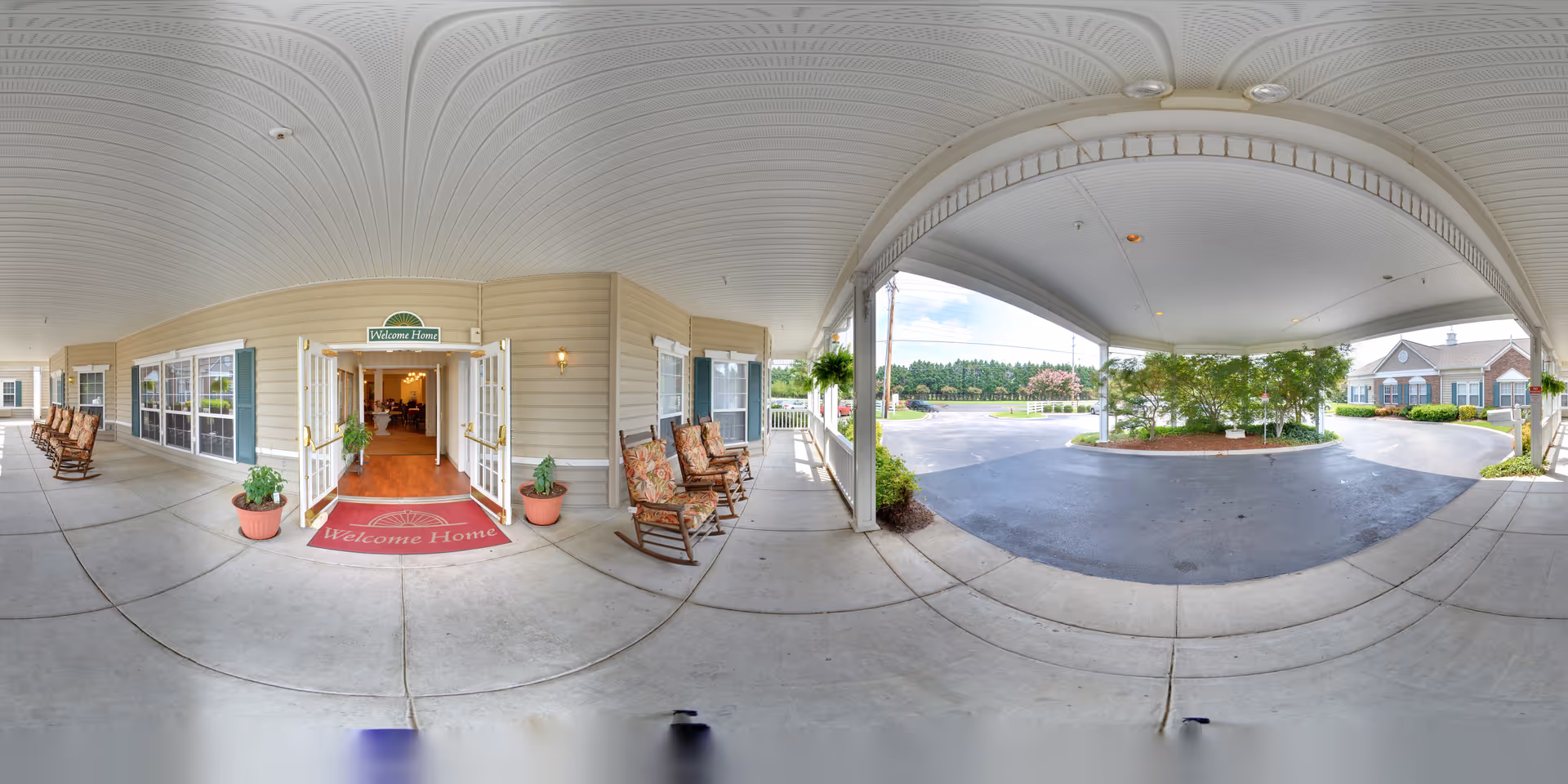 Covered front entrance and drive-through canopy of Morningside of Decatur with rocking chairs, potted plants, a "Welcome Home" mat and double doors opening into the building.