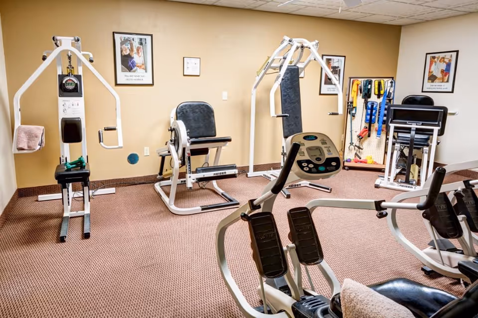 Small fitness room with several exercise machines and resistance bands on a carpeted floor.