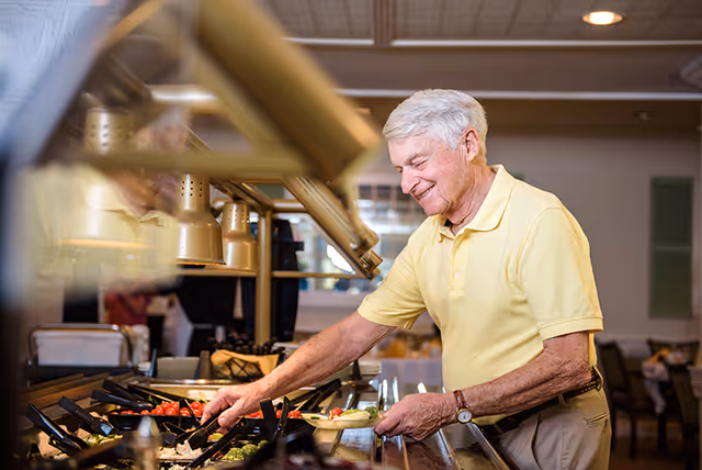 An elderly man serving himself from a buffet salad bar in a dining area.