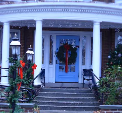 Blue front door with white columns, wreath, and festive holiday decorations at entrance.