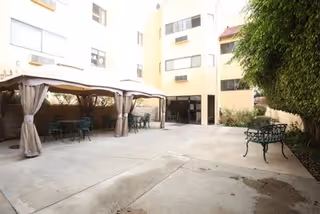 Enclosed courtyard with canopy-covered seating, metal tables and chairs, and the building entrance in the background.