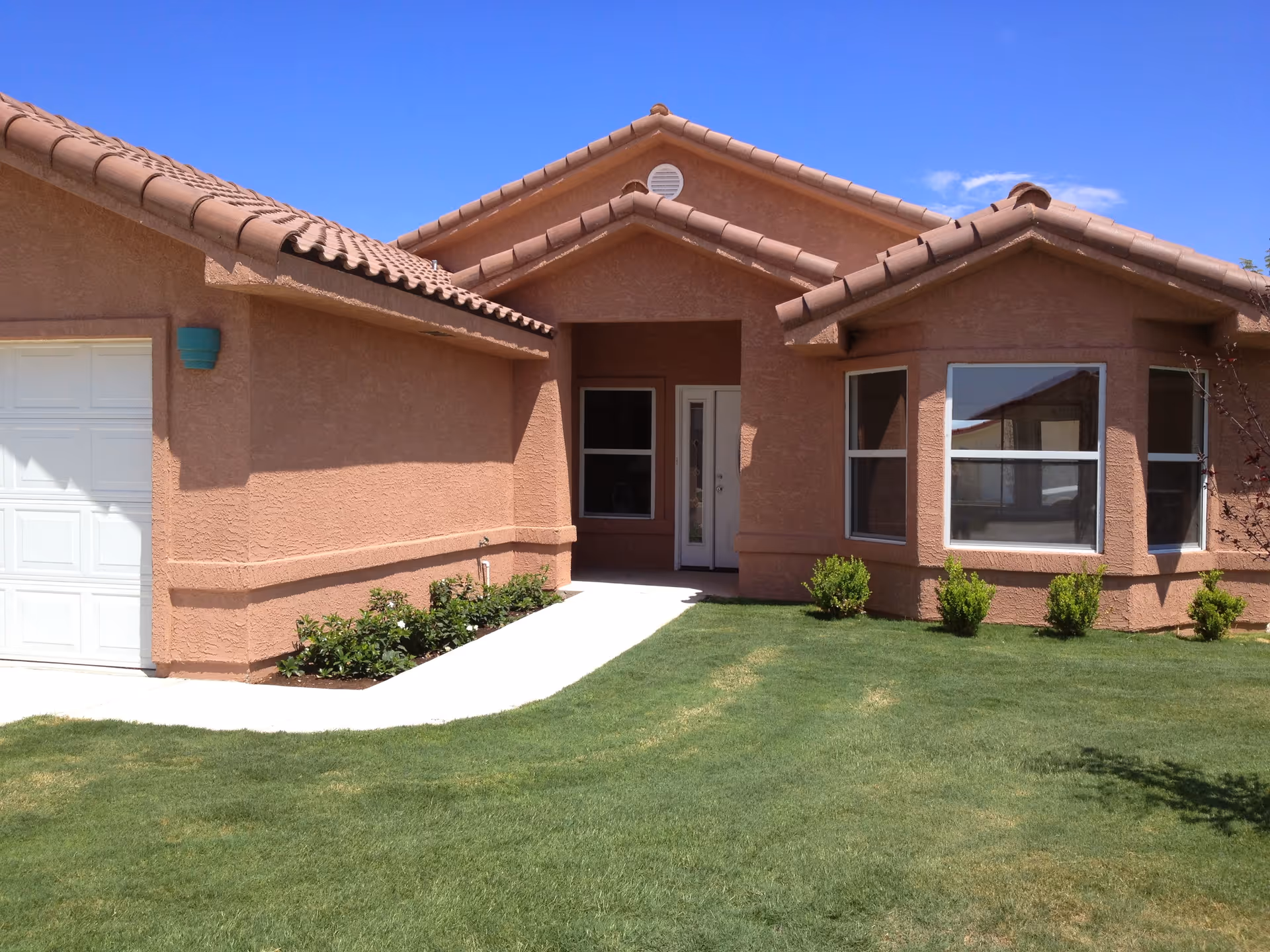 Front exterior of a single-story stucco house with a tiled roof, garage, walkway and green lawn.