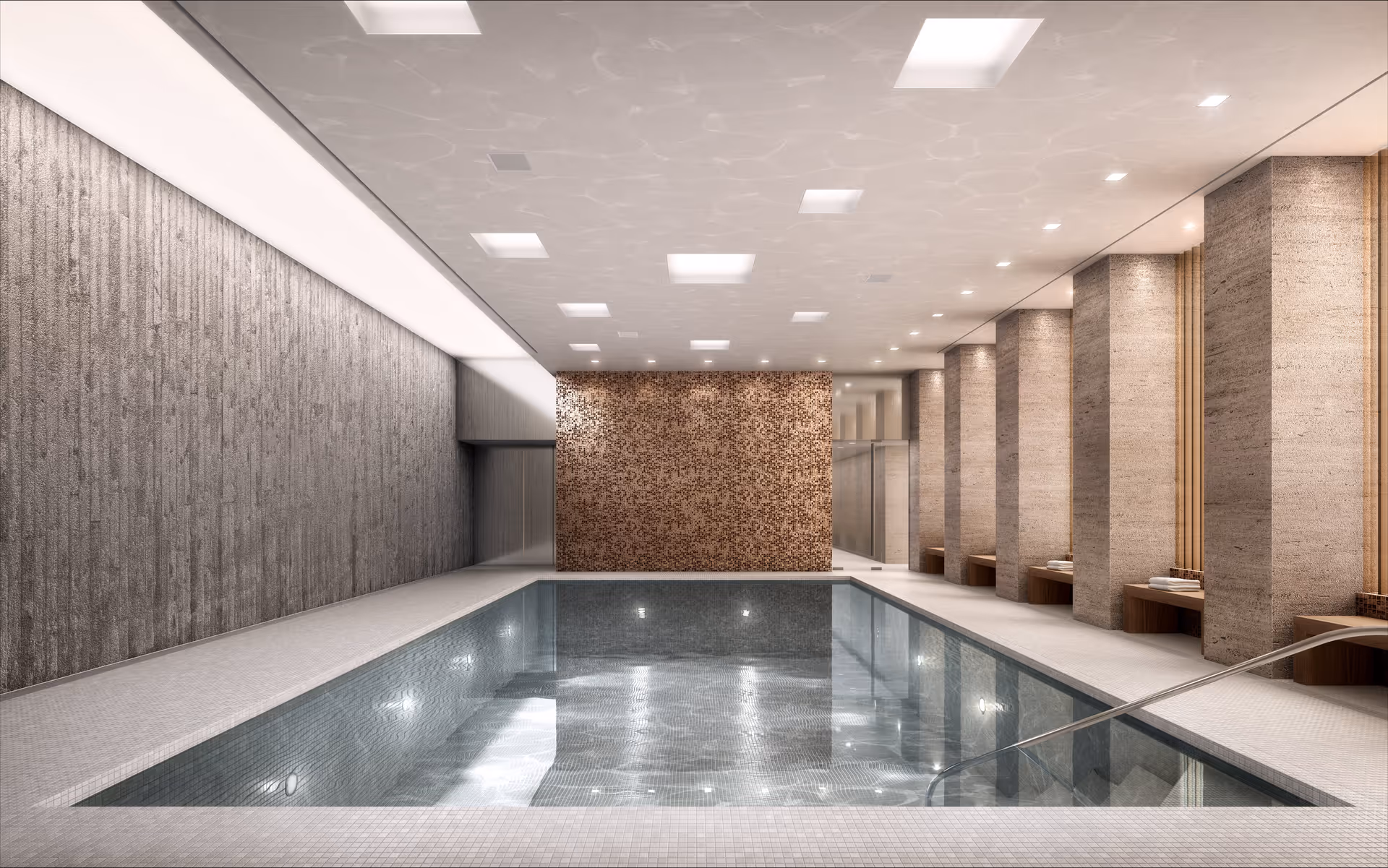 Indoor swimming pool with clear water, surrounded by textured walls and columns. The ceiling has recessed lighting, and there are benches along the right side near the columns. The pool area has a modern and clean design with a calm atmosphere.