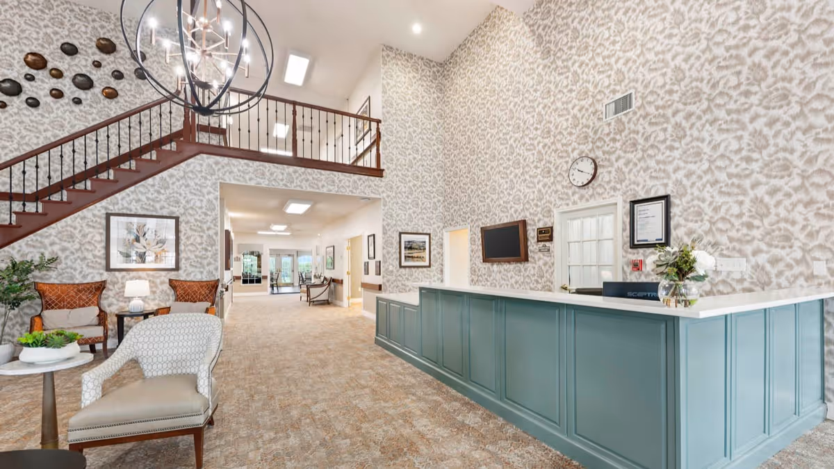 Spacious reception lobby with a long teal front desk, seating area, staircase, and patterned wallpaper.