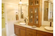 Bright bathroom with a wooden double-sink vanity, vessel sinks, mirrored cabinets and towel rings.