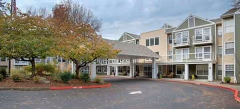 Exterior view of Brookdale River Valley Tualatin's entrance with a covered driveway and trees.