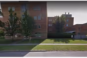 Exterior view of a multi-story brick nursing facility with a grass lawn, trees, and a sidewalk in front.
