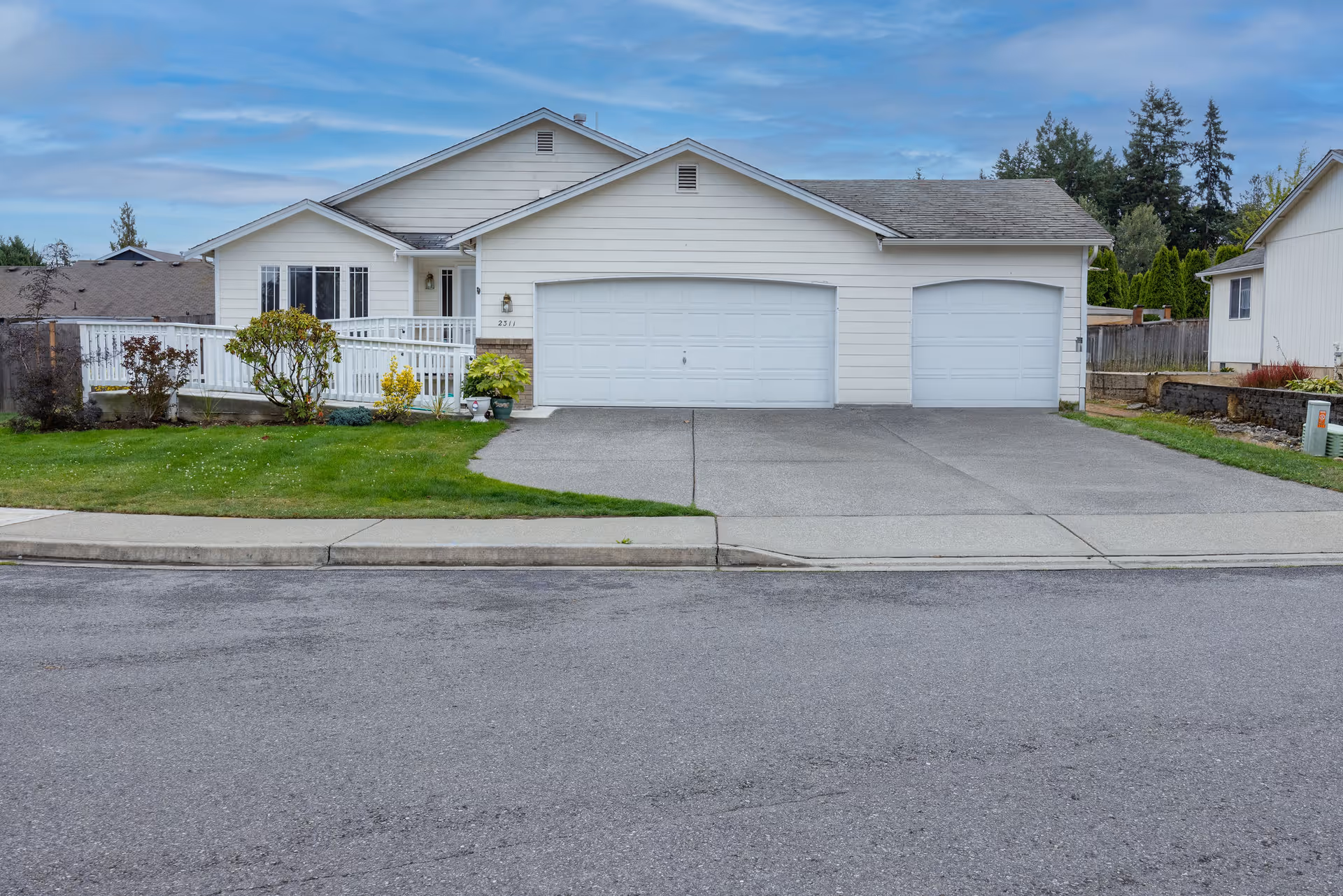 Single-story white house with a three-car garage, front lawn, and driveway under a cloudy sky.