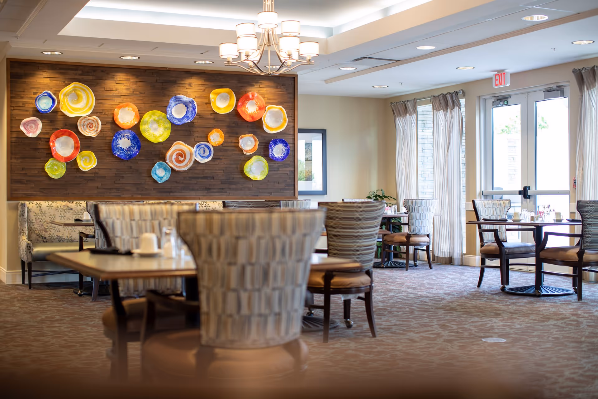 Bright dining room with tables and upholstered chairs and colorful circular glass wall art.