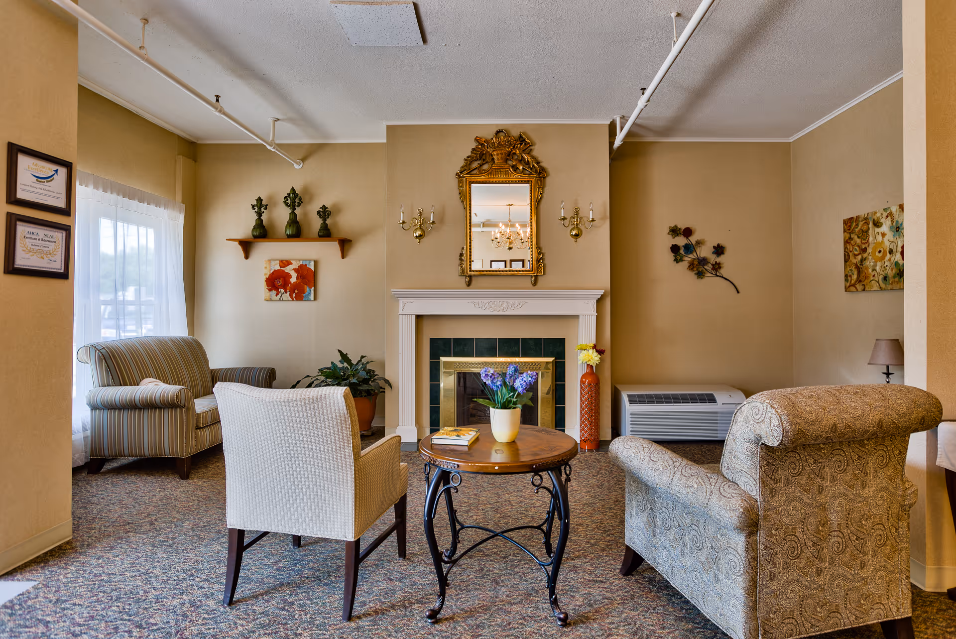 Cozy seating area with armchairs and a small round table in front of a decorative fireplace and mirror.