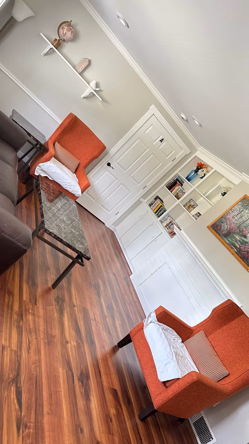 Cozy living room with two orange armchairs, a marble-top coffee table, built-in white shelving, and wood floors.