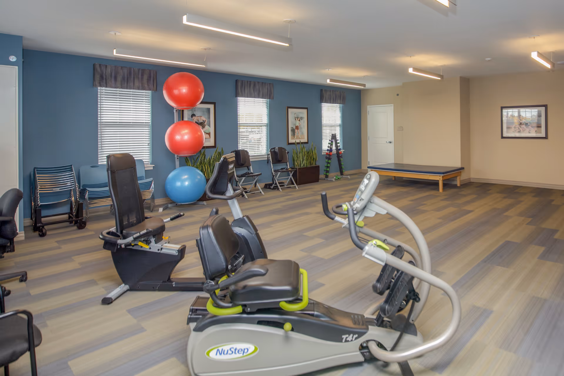 Interior fitness room with recumbent exercise machines, large stability balls, chairs and a stretching table.