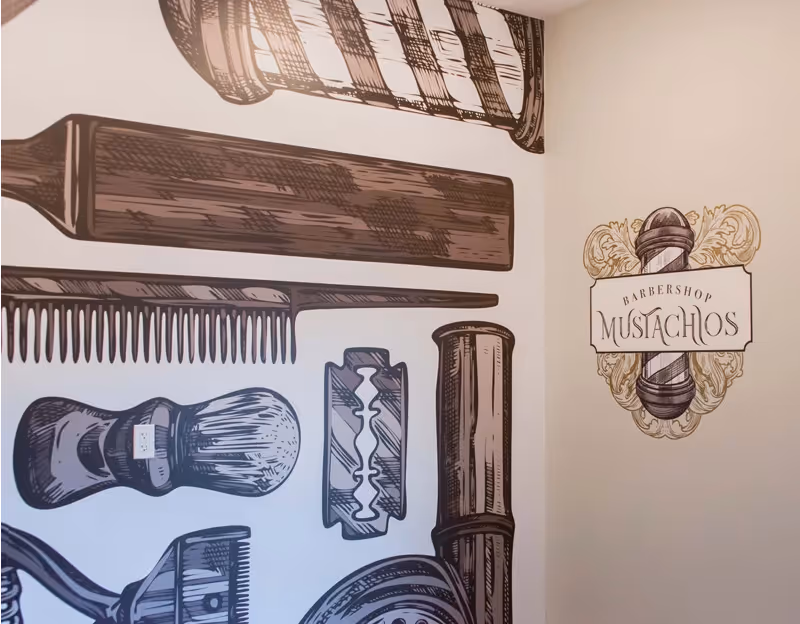 Wall mural featuring vintage barbershop tools including a straight razor, comb, shaving brush, razor blade, and a barber pole with the text 'Barbershop Mustachios'.