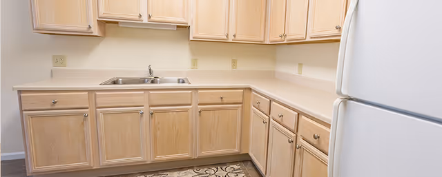 L-shaped kitchen with light wood cabinets, laminate countertops, a double sink, and a white refrigerator.