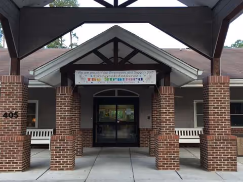 Brick-front entrance to The Stratford senior living facility with benches and a banner sign.