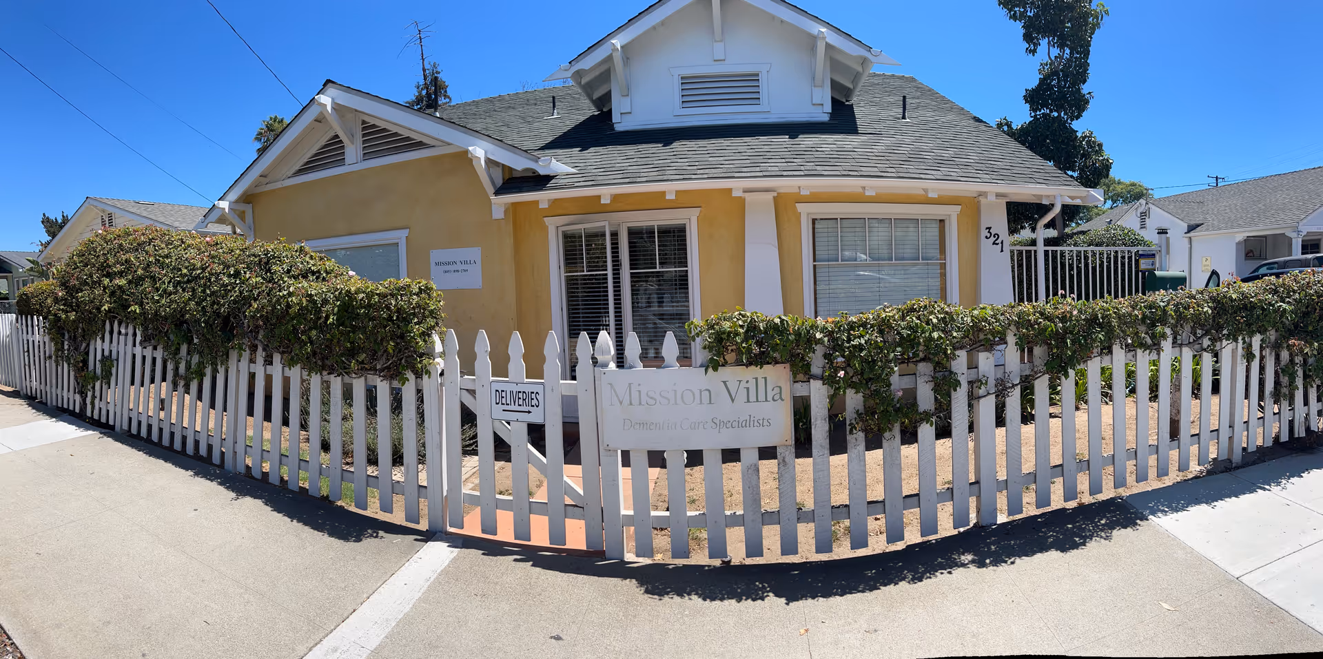 Front view of a yellow single-story house with a white picket fence and a sign reading 'Mission Villa'.