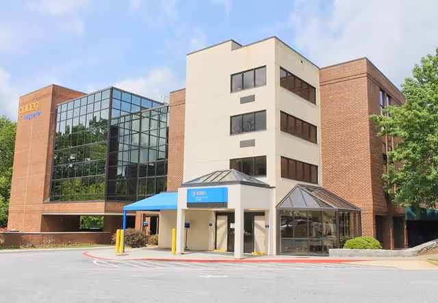 Exterior view of a multi-story senior living facility with brick, glass facade and blue entrance awning.