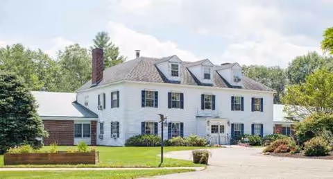 White colonial-style senior living building with manicured lawn and driveway.