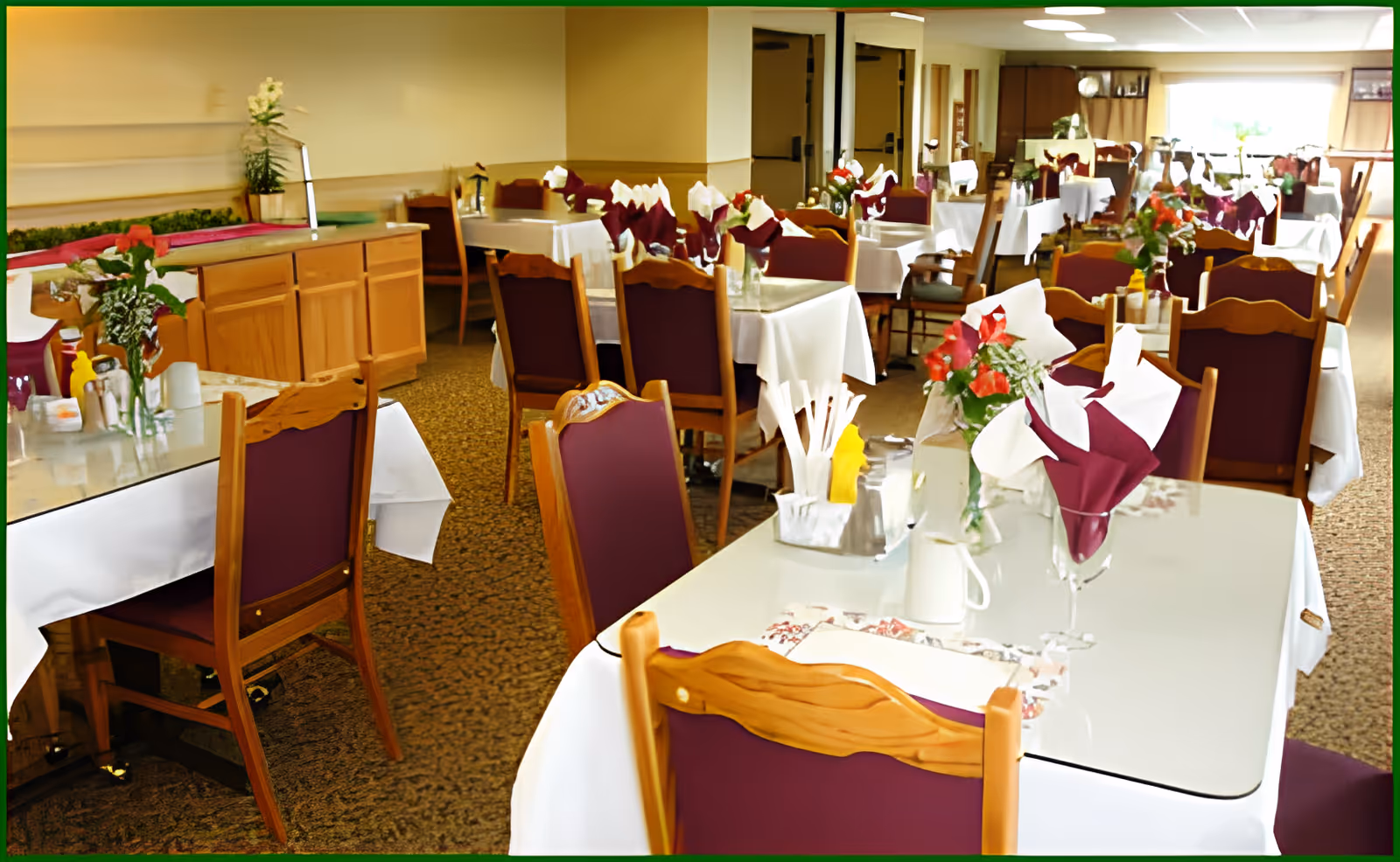 Dining room with multiple tables set with white tablecloths, folded napkins, and floral centerpieces.