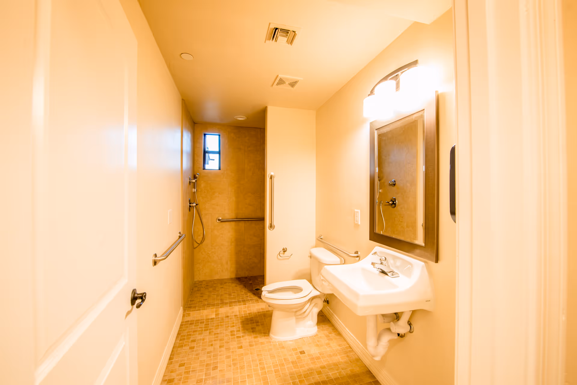 Accessible bathroom with a wall-mounted sink, toilet, grab bars, mirror, and a walk-in shower.