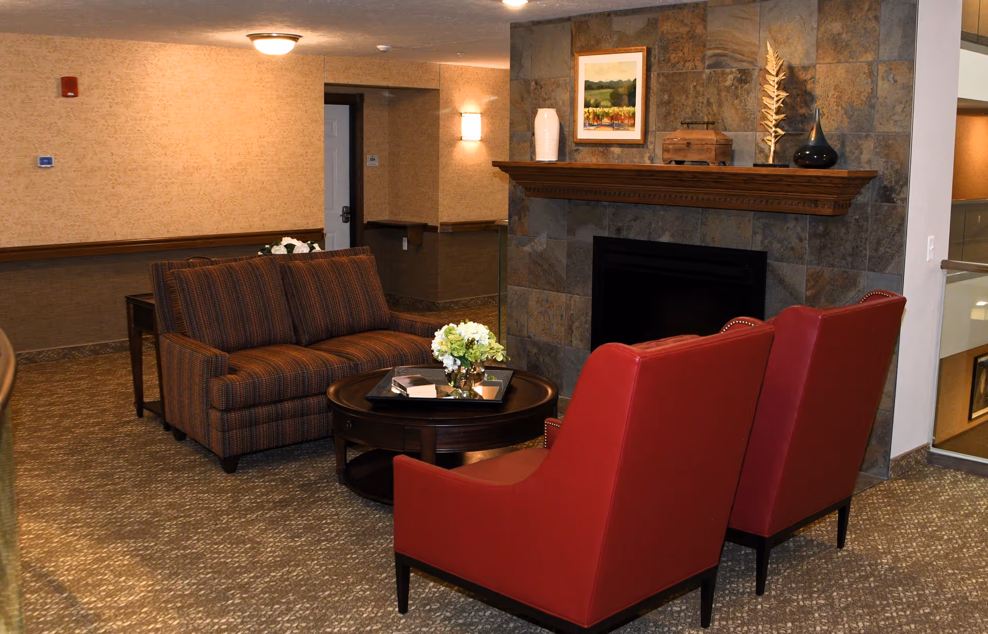 Cozy sitting area with a sofa, two red armchairs, a round coffee table and a fireplace in a lounge.