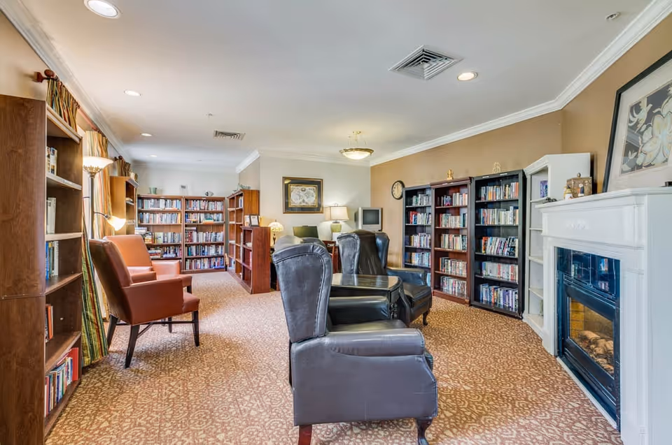 Cozy common room with bookshelves, armchairs and leather chairs arranged around a fireplace and reading area.