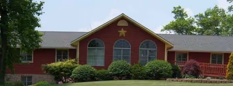 Red building with arched windows and star on facade, surrounded by shrubs.