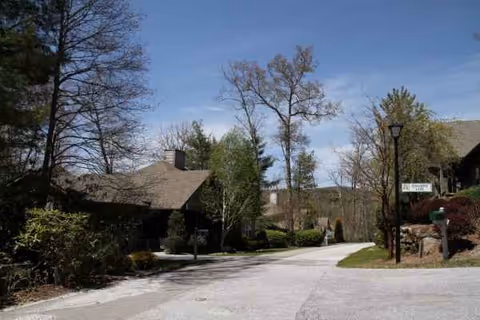 Curved driveway leads to a low stone-clad senior living building surrounded by trees.