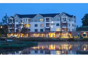 Exterior view of a multi-story senior living facility named Asbury Place Maryville at dusk, with lights glowing from the windows and a calm pond reflecting the building in the foreground.