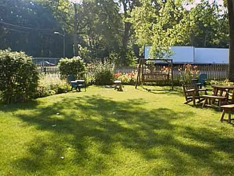 Sunny outdoor yard with green grass, benches, tables, and a wooden fence.