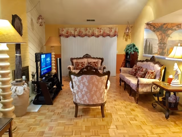 A cozy senior living room with sofas, armchairs, a TV, and warm lighting.