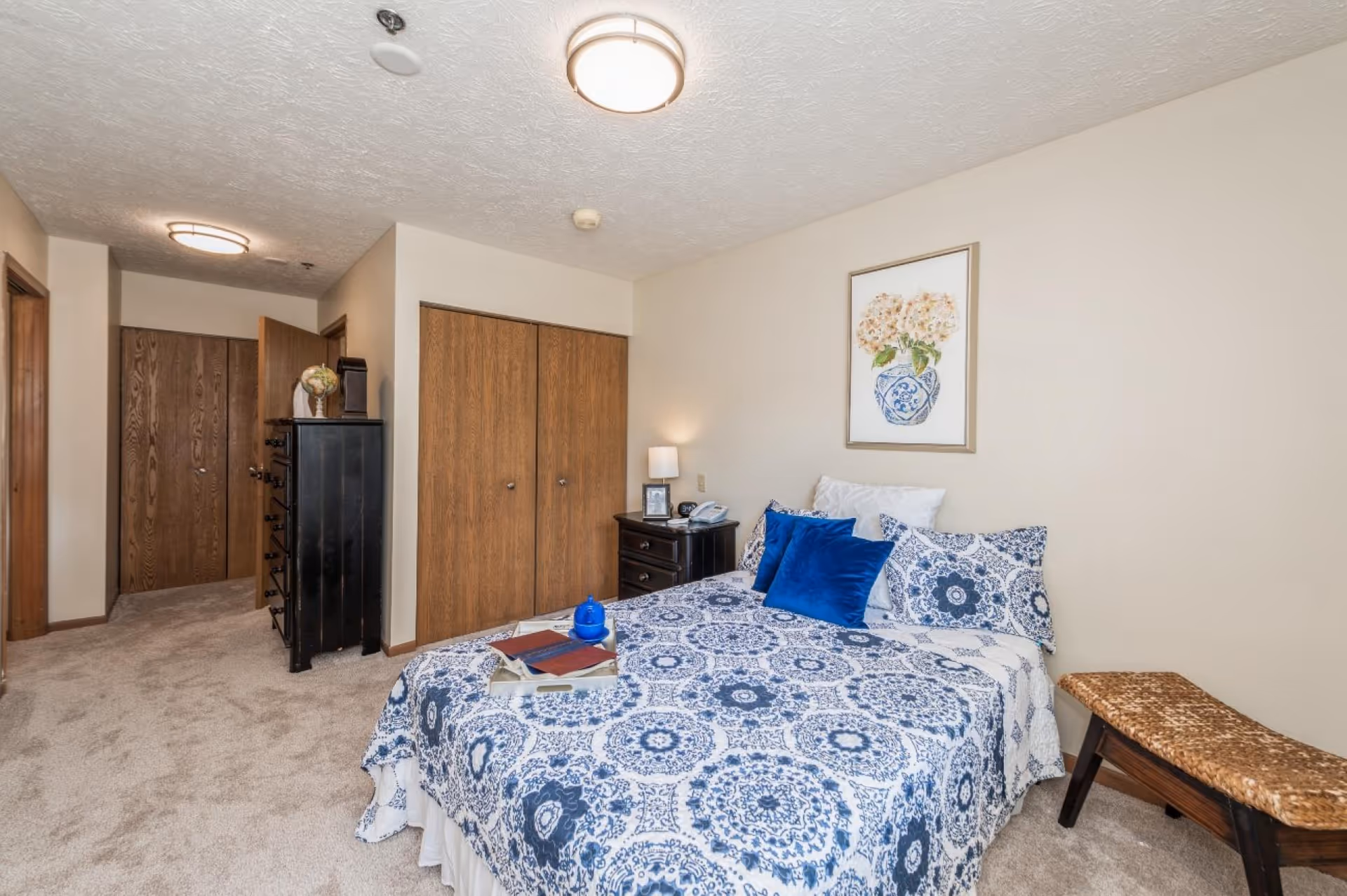 A bedroom with a bed dressed in blue patterned bedding, a nightstand, dresser, and wooden closet doors.