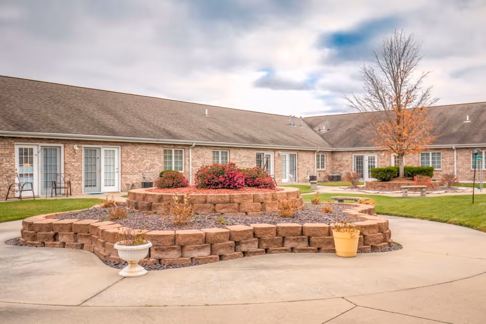 Brick single-story senior living building surrounding a landscaped courtyard with a tiered stone planter, potted plants, and walkways.