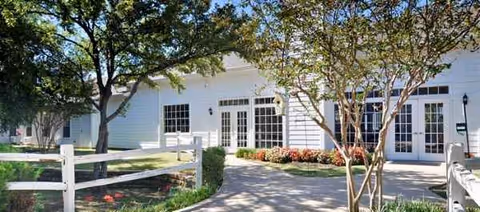 White facility entrance with glass doors, windows, and manicured landscaping.