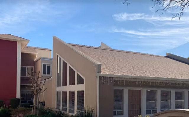 Exterior view of a senior living facility building with a sloped roof, large triangular windows, and beige and red walls under a blue sky.