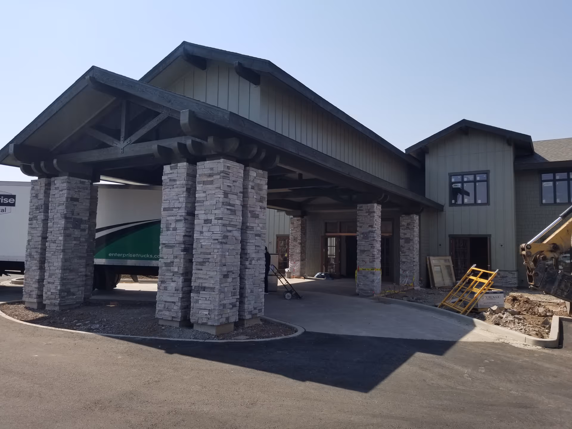 Covered entrance of a senior living building with stone pillars, construction equipment, and a delivery truck.