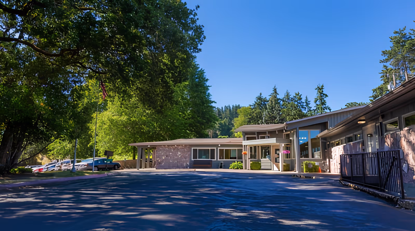 Exterior view of Hillside Heights Rehabilitation Center building surrounded by tall green trees under a clear blue sky, with a parking area visible to the left.