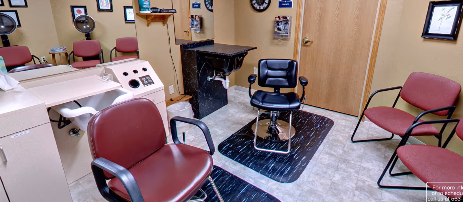 Small salon room with maroon waiting chairs, a black styling chair on a mat, a shampoo sink and mirrors.